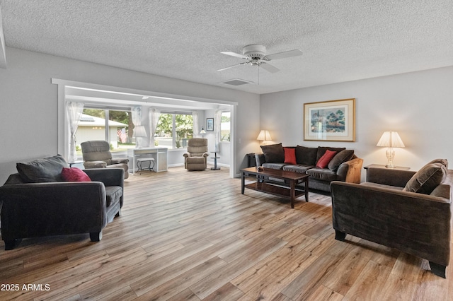 living room featuring light wood-type flooring, a ceiling fan, visible vents, and a textured ceiling