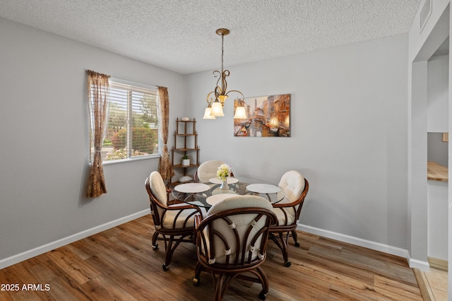 dining space featuring a textured ceiling, wood finished floors, visible vents, and a notable chandelier