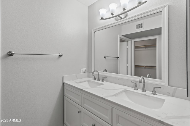 bathroom with double vanity, a textured wall, visible vents, and a sink