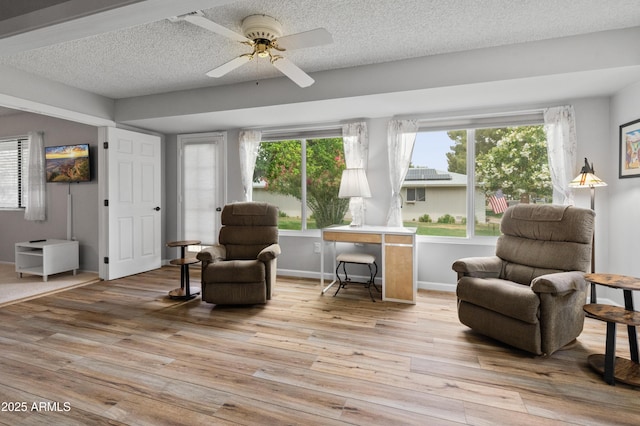living area featuring a textured ceiling, light wood-style flooring, a healthy amount of sunlight, and ceiling fan