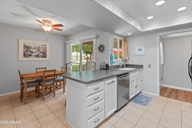 kitchen featuring white cabinets, a sink, dark countertops, crown molding, and dishwasher