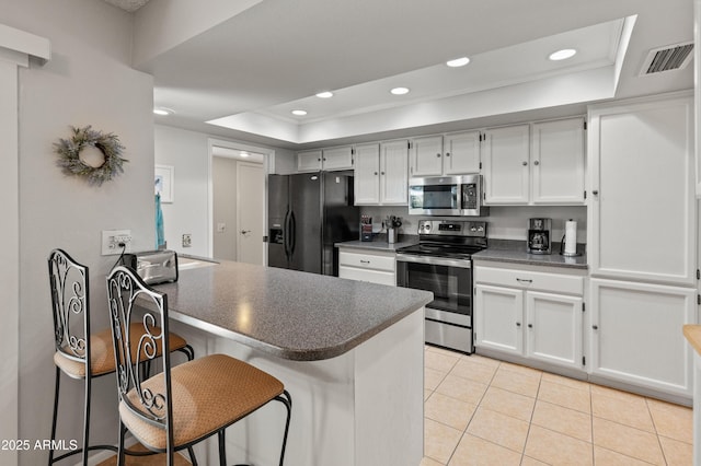 kitchen featuring dark countertops, light tile patterned floors, a raised ceiling, a peninsula, and appliances with stainless steel finishes