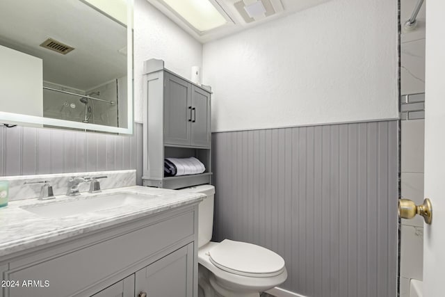 full bath featuring toilet, vanity, visible vents, wainscoting, and walk in shower