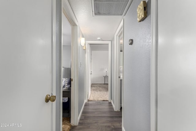 hallway featuring a textured ceiling, a textured wall, visible vents, baseboards, and dark wood finished floors