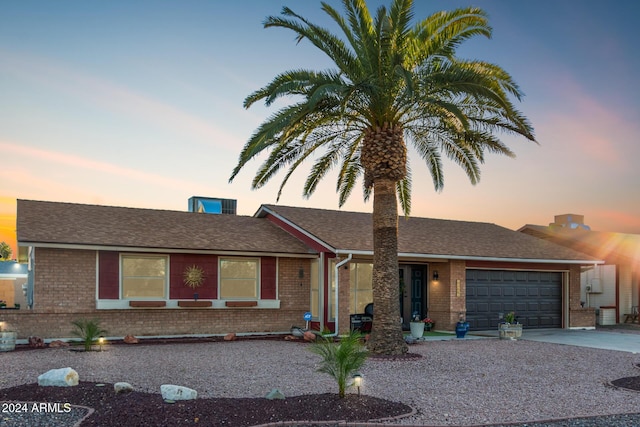 ranch-style house featuring driveway, an attached garage, roof with shingles, and brick siding