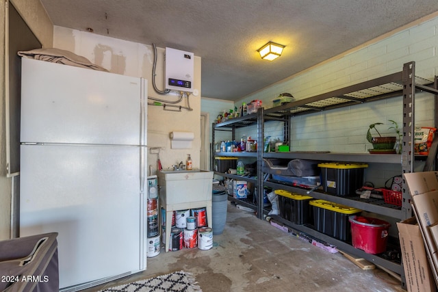 interior space with concrete block wall, a textured ceiling, unfinished concrete flooring, and freestanding refrigerator