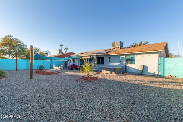 back of house featuring a fenced backyard, a jacuzzi, cooling unit, a patio area, and roof mounted solar panels