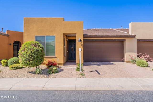 adobe home with decorative driveway, an attached garage, and stucco siding