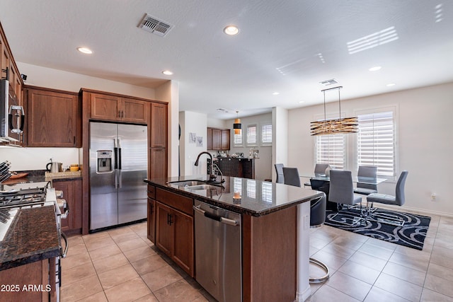 kitchen with appliances with stainless steel finishes, a sink, dark stone countertops, light tile patterned floors, and visible vents
