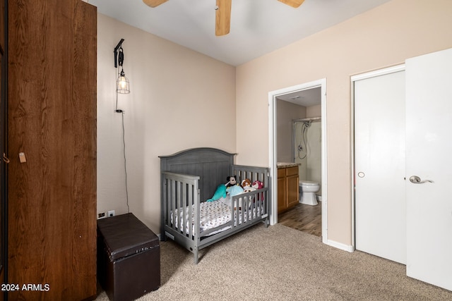 bedroom with a crib, carpet flooring, ceiling fan, and ensuite bathroom