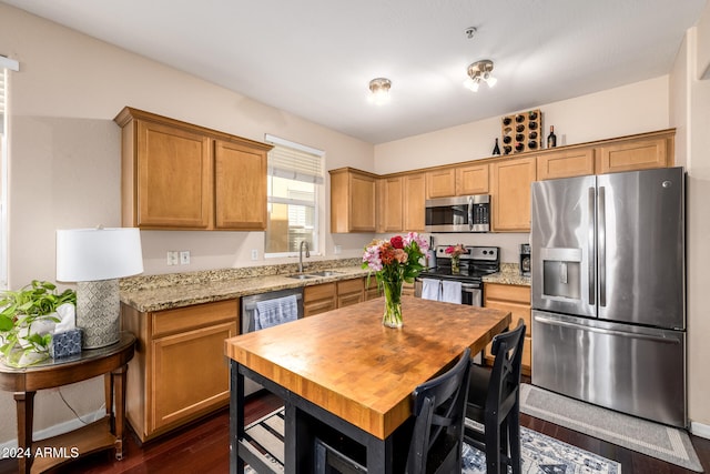 kitchen with light stone counters, sink, appliances with stainless steel finishes, and dark wood-type flooring