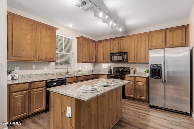 kitchen with hardwood / wood-style flooring, sink, black appliances, light stone countertops, and a center island