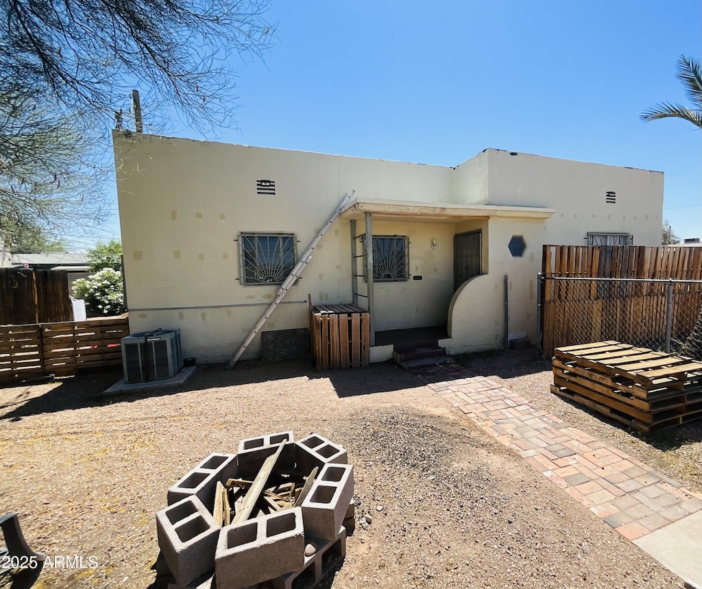rear view of house featuring fence, an outdoor fire pit, central AC unit, and stucco siding