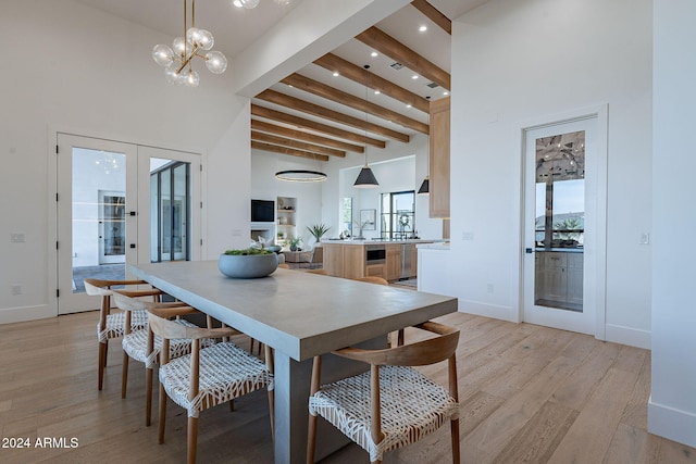 dining space with french doors, light hardwood / wood-style floors, beam ceiling, an inviting chandelier, and a towering ceiling