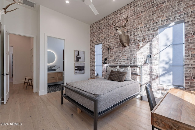 bedroom with light hardwood / wood-style floors, ensuite bathroom, brick wall, and ceiling fan