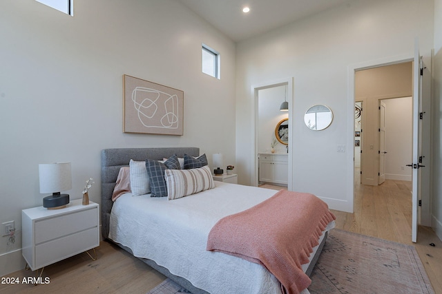 bedroom featuring ensuite bath, light hardwood / wood-style flooring, and a high ceiling