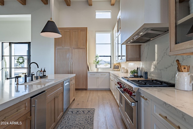 kitchen with wall chimney range hood, appliances with stainless steel finishes, white cabinets, beam ceiling, and light hardwood / wood-style flooring