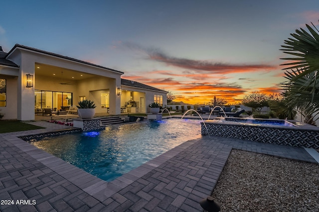 pool at dusk featuring an in ground hot tub, a patio area, pool water feature, and ceiling fan