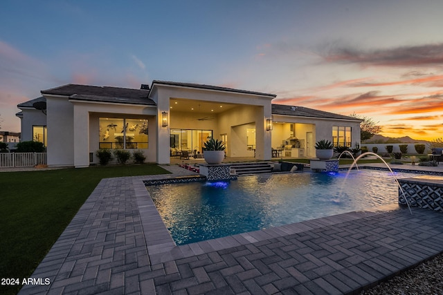 back house at dusk with a patio, pool water feature, and a lawn