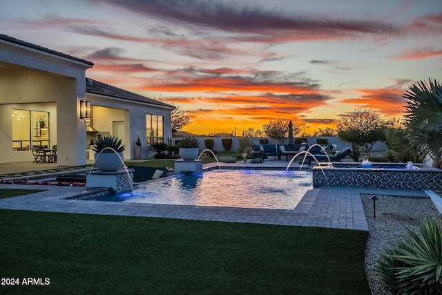 pool at dusk with a patio, pool water feature, and a lawn