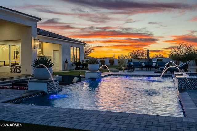 pool at dusk featuring a patio, an outdoor living space, and pool water feature