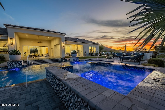 pool at dusk featuring a hot tub, an outdoor living space, pool water feature, and a patio