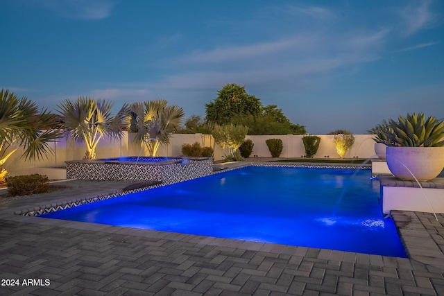 pool at dusk with pool water feature and a patio area