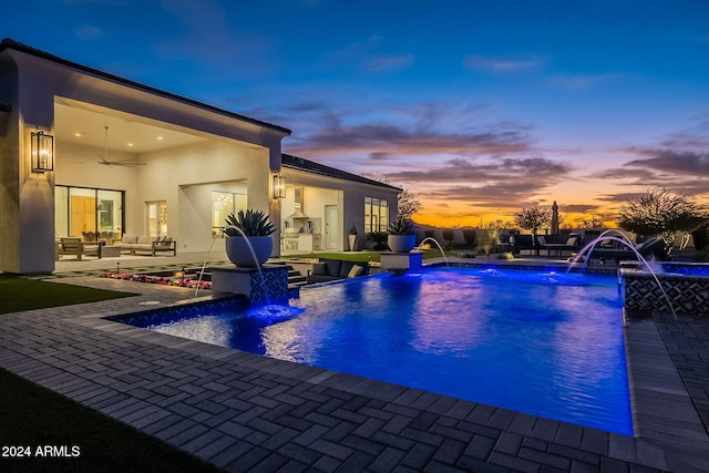 pool at dusk with a patio, pool water feature, and an outdoor hangout area