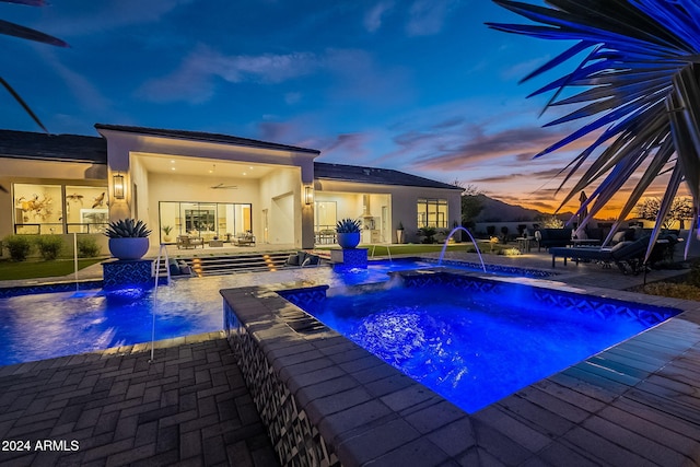 pool at dusk with a patio, pool water feature, and a jacuzzi