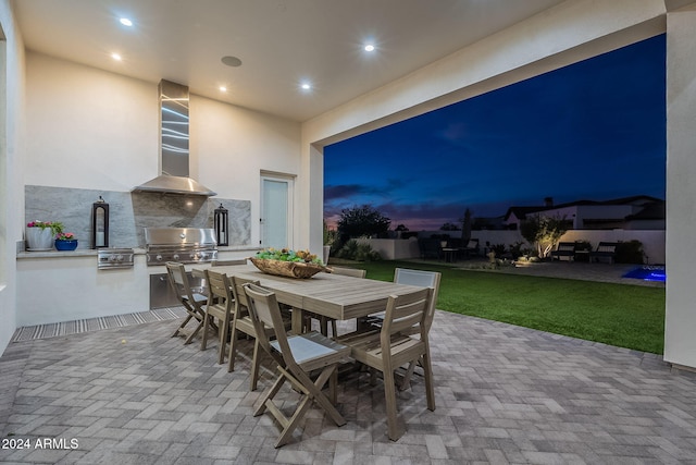 patio terrace at dusk with a yard, grilling area, and exterior kitchen