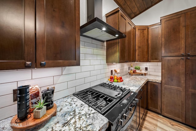 2702 Majestic Elk Rd, Overgaard, AZ 85933 - kitchen featuring tasteful backsplash, black range with gas cooktop, wall chimney range hood, light stone countertops, and light wood-style flooring