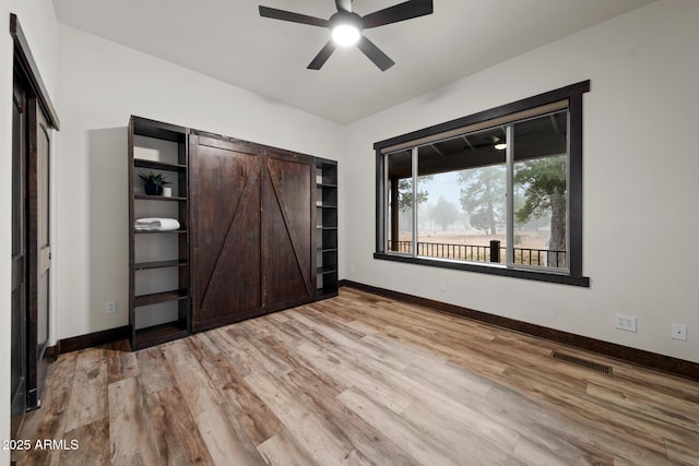 2702 Majestic Elk Rd, Overgaard, AZ 85933 - unfurnished bedroom featuring baseboards, a ceiling fan, a barn door, light wood-style floors, and visible vents
