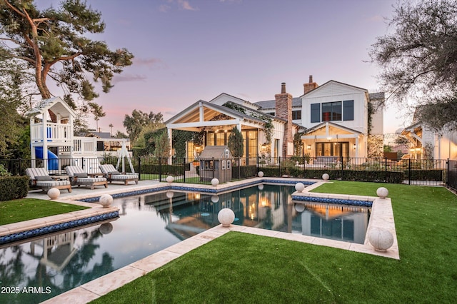 back of property at dusk featuring a fenced in pool, a patio, a chimney, fence, and a yard