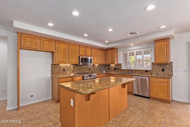 kitchen with a kitchen island, stainless steel appliances, dark stone counters, sink, and light tile patterned floors