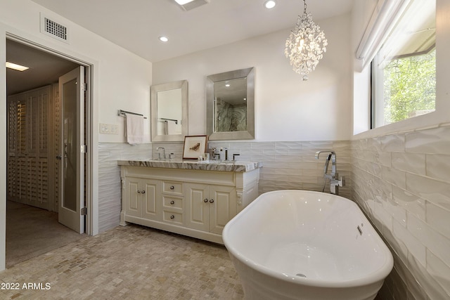 bathroom featuring a notable chandelier, a washtub, tile walls, and vanity