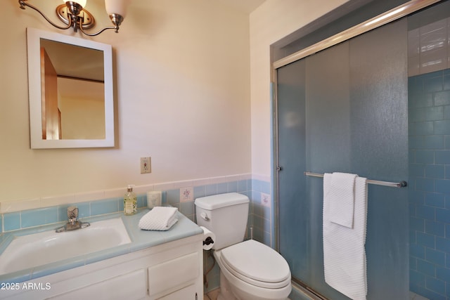 bathroom featuring vanity, toilet, a shower with shower door, and tile walls