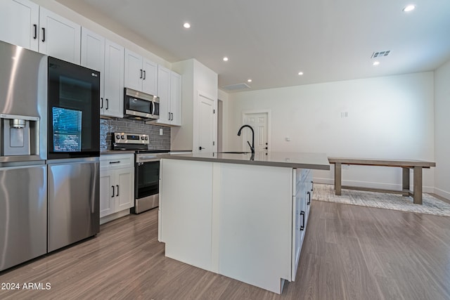 kitchen with tasteful backsplash, light wood-type flooring, white cabinetry, stainless steel appliances, and a center island with sink