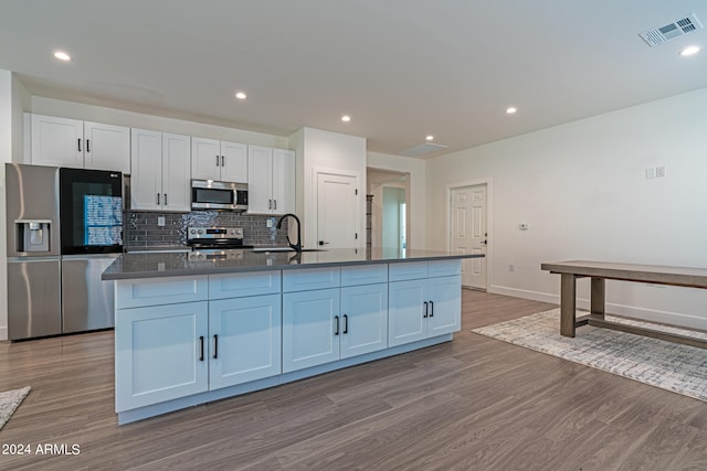 kitchen with appliances with stainless steel finishes, light hardwood / wood-style flooring, an island with sink, and white cabinets