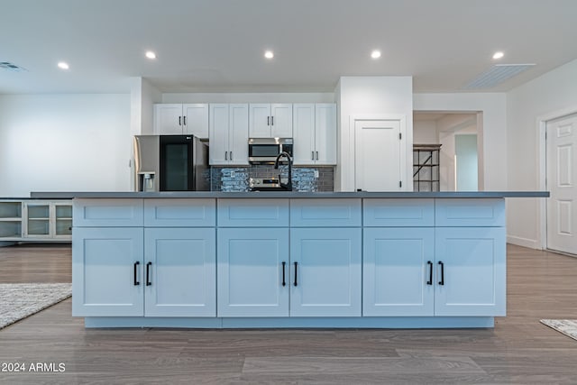 kitchen featuring a spacious island, stainless steel appliances, backsplash, light wood-type flooring, and white cabinetry