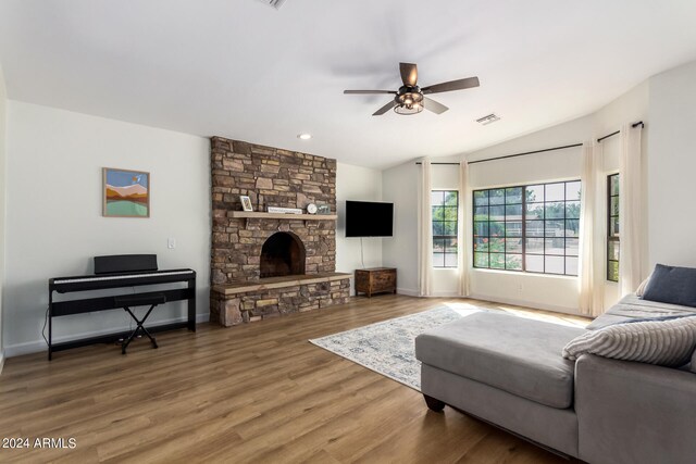 living room with ceiling fan, a stone fireplace, hardwood / wood-style floors, and vaulted ceiling