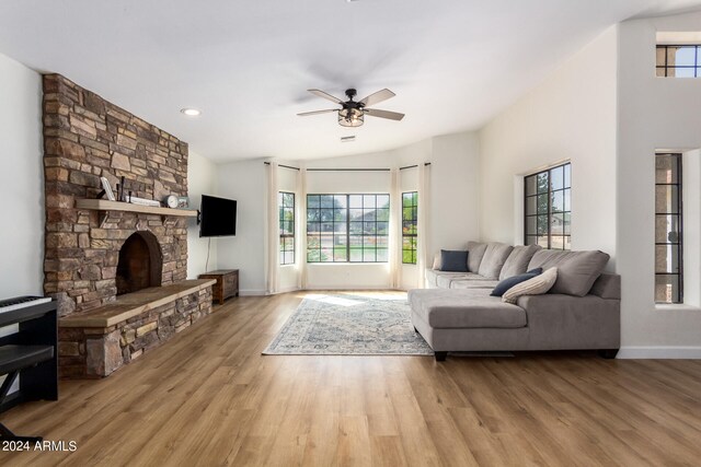 living room featuring ceiling fan, light wood-type flooring, plenty of natural light, and a stone fireplace