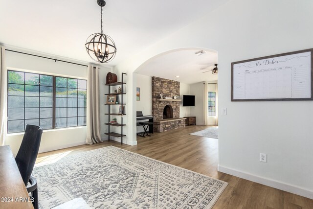 office area with ceiling fan with notable chandelier, hardwood / wood-style flooring, a fireplace, and vaulted ceiling