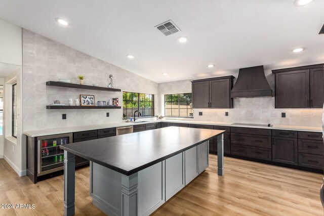 kitchen with custom exhaust hood, beverage cooler, light hardwood / wood-style flooring, and a center island