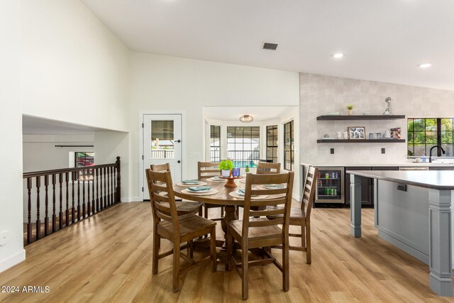 dining room with high vaulted ceiling, wine cooler, light hardwood / wood-style flooring, and sink