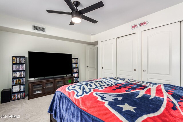 bedroom with ceiling fan, light colored carpet, and multiple closets