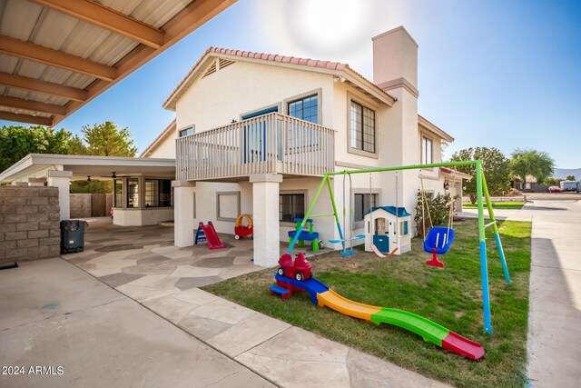 rear view of house with a playground, a balcony, and a patio