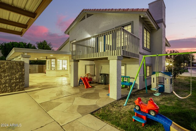 back house at dusk featuring a playground, a balcony, and a patio