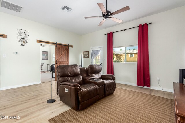 living room featuring a barn door, light hardwood / wood-style floors, and ceiling fan