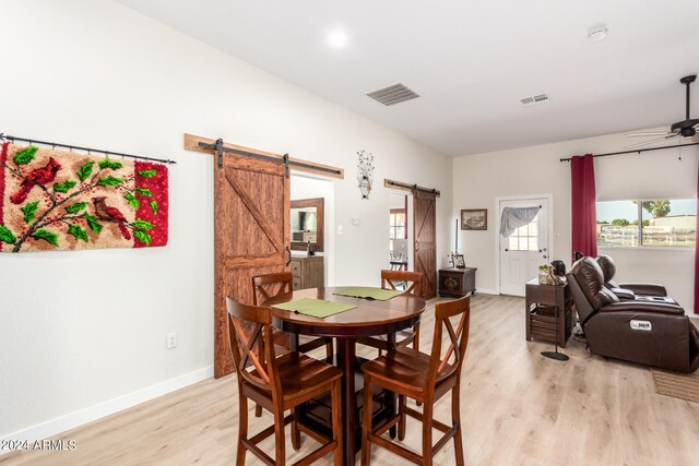 dining area with ceiling fan, a barn door, and light hardwood / wood-style flooring