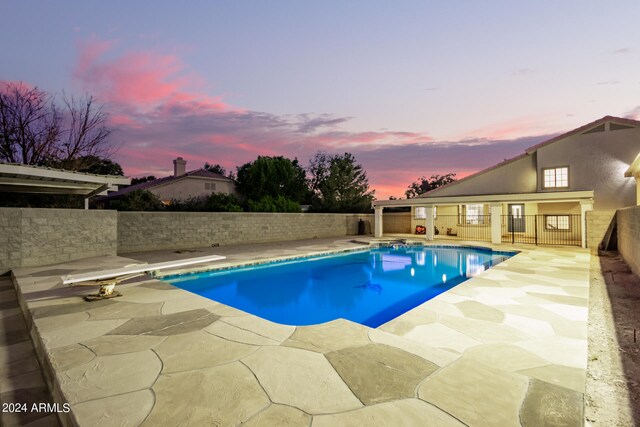 pool at dusk featuring a diving board and a patio area